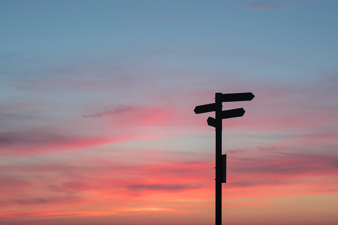 Direction signs against sunset sky